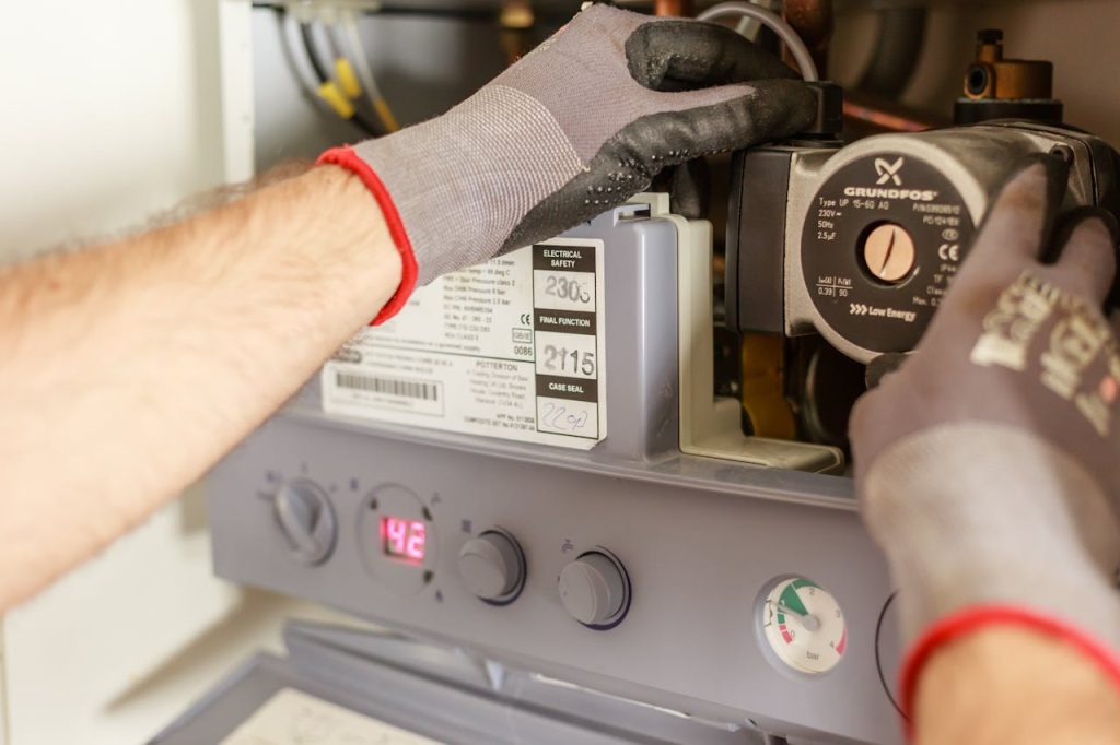 plumber-repairing-power-source-7859953 Close-up of hands adjusting a boiler system with precise instrumentation, showing maintenance work.